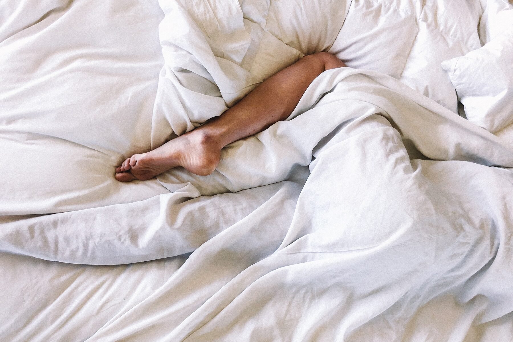 Woman wrappend in white sheet on he bed, only her leg is showing