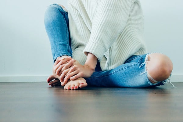 Woman in jeans and white sweather sitting on the floor barefoot