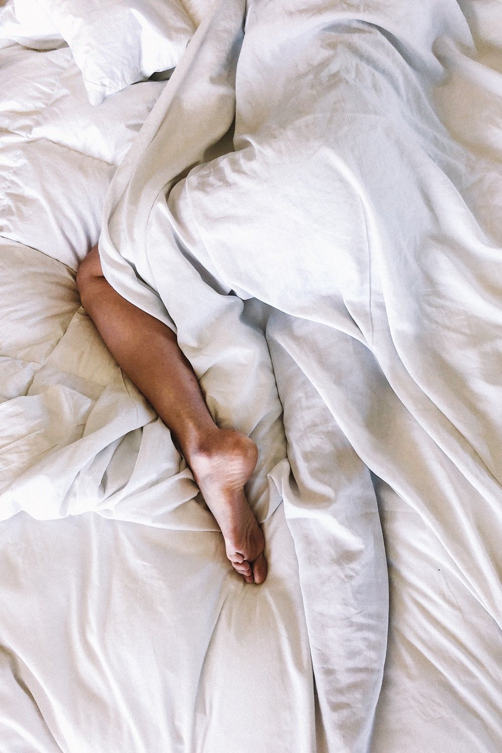 Woman on bed wrapped in sheets, ony one leg is showing